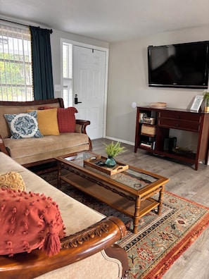 A living room with a sofa, coffee table, TV, and a bookshelf. - Boho Chic Home (New port richey)