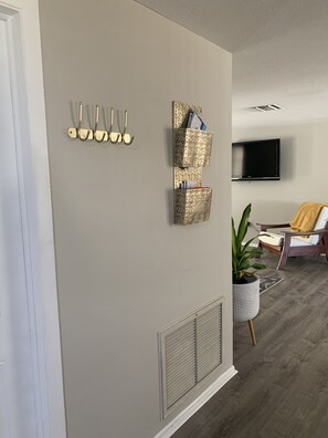 A living room with a grey wall, a mounted TV, a plant, and a chair with a yellow cushion.