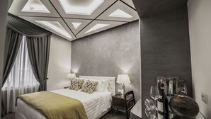 A modern hotel room with a geometric ceiling design, a large bed with a green throw, two bedside tables with lamps, and a minibar with wine glasses. - Spagna Boutique Luxury Suites (Rome)