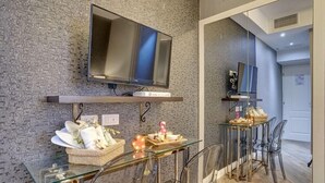A modern bathroom with a glass vanity, a flat-screen TV mounted on the wall, and a mirror above the vanity. - Spagna Boutique Luxury Suites (Rome)