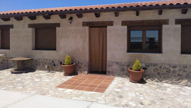 A building with a tiled roof, a wooden door, and two windows with shutters. There are two potted plants in front of the windows. - La Carrascala rural house 2 (Villaseco del Pan)