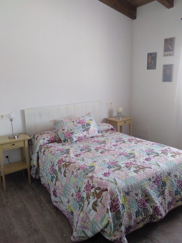 A bedroom with a floral bedspread, wooden headboard, bedside tables with lamps, and a wall with framed pictures.