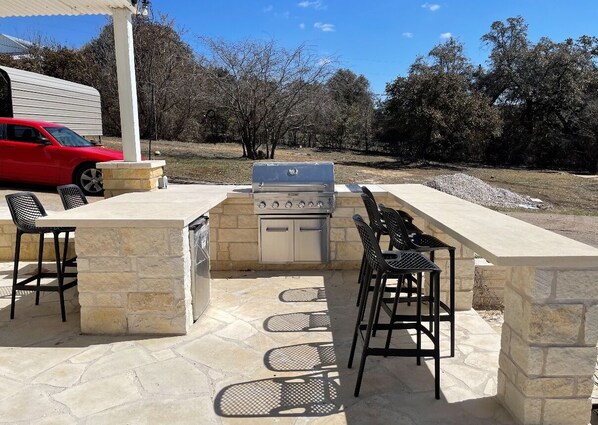 An outdoor patio with a stone barbecue grill, seating area, and a red car parked nearby. - Luxury Lake Travis Escape with Lake Access! (Leander)
