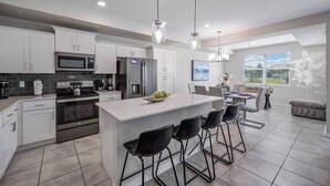 A modern kitchen with white cabinets, stainless steel appliances, and a central island with bar stools.