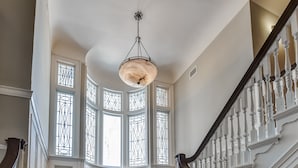 A grand staircase with white balusters and a dark handrail, leading to a landing with a large, ornate chandelier.