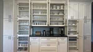 A kitchen with white cabinetry, open shelves with glassware and plates, and a coffee maker on the counter.