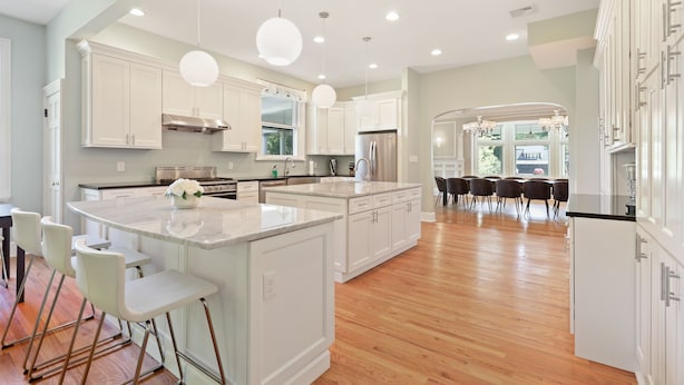 A modern kitchen with white cabinetry, a large island with bar stools, and a dining area with a chandelier.