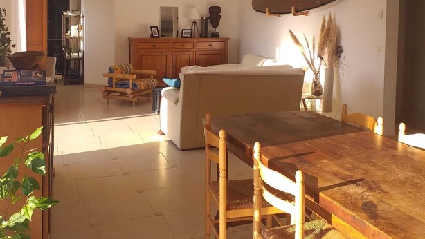 A spacious living area with a wooden dining table, a sofa, and a kitchen in the background. - HOUSE Assérac, Pen Bé, quiet, Near beaches, 10m from coastal path (Assérac)