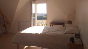 A bedroom with a bed, a nightstand, a lamp, and a window with a view of the outdoors. - HOUSE Assérac, Pen Bé, quiet, Near beaches, 10m from coastal path (Assérac)