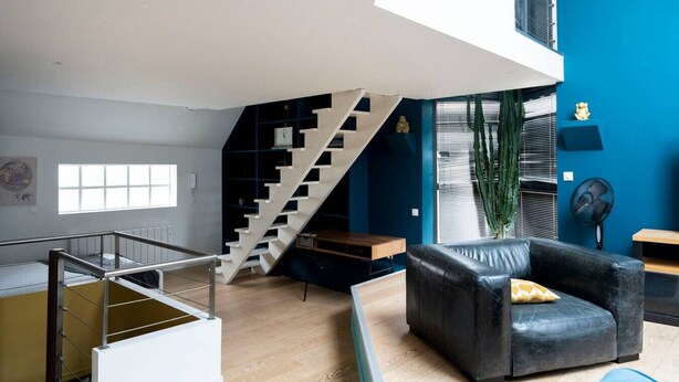 Un interior modern amb una escala, un sofà de pell negra i una finestra gran.