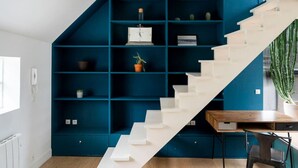 Un interior modern amb una escala blanca, prestatges color turquesa i una zona de menjador.