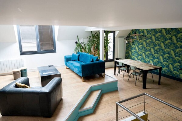 A modern living room with a blue sofa, a wooden dining table, and a staircase.