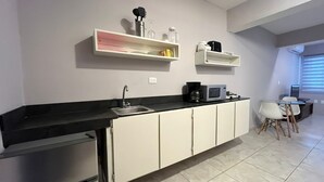 Een moderne keuken met een zwart aanrecht, witte kasten, een inbouwspoelbak en een magnetron. In het aangrenzende eetgedeelte staan witte stoelen en een kleine eettafel.