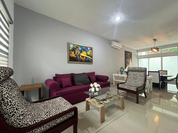 A modern living room with a sofa, armchair, coffee table, and artwork on the wall.