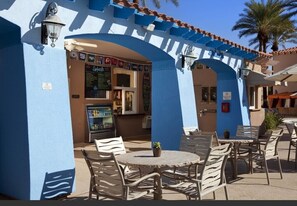 Enjoy a meal under the shade of a blue awning, surrounded by palm trees and traditional Mediterranean architecture.
