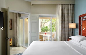 Relax in this serene space with a large bed against a window, a sliding door leading to an outdoor area with a table and chairs, and a TV mounted on the wall.