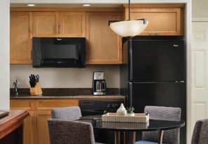 Compact kitchen with a refrigerator, microwave, and coffee maker, perfect for preparing meals. A dining table with two chairs and a vase complete the space.