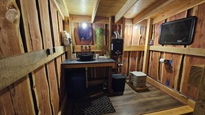 A compact kitchen with wooden walls, a sink, a stove, and a small trash bin. - GlampVentures "Cedar Suncatcher" @river/lake near Smoky Mtns  (Newport)