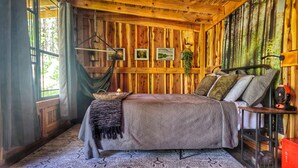 Una habitación tipo cabaña de madera con una cama, un sillón colgante y una ventana con cortinas.