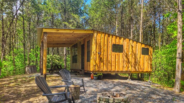 Una cabaña de madera con un porche cubierto, dos sillas Adirondack y un brasero.