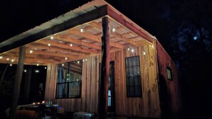 Una cabaña de madera con un porche cubierto, ventanas amplias y luces colgantes.