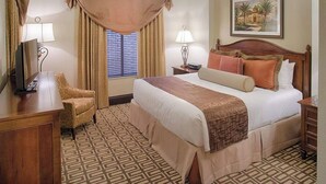 A hotel room with a large bed, two bedside lamps, a desk with a chair, and a window with curtains.
