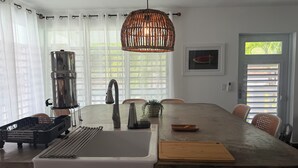Una cocina con una isla grande, un dispensador de agua de acero inoxidable, una lámpara colgante y una puerta con vista a una ventana.