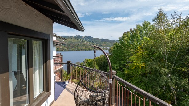 Un balcon avec un fauteuil suspendu, une vue sur un lac et une végétation luxuriante tout autour.