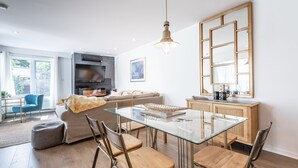 Un salon moderne avec une table à manger en verre, des chaises en bois, un canapé et un grand miroir.