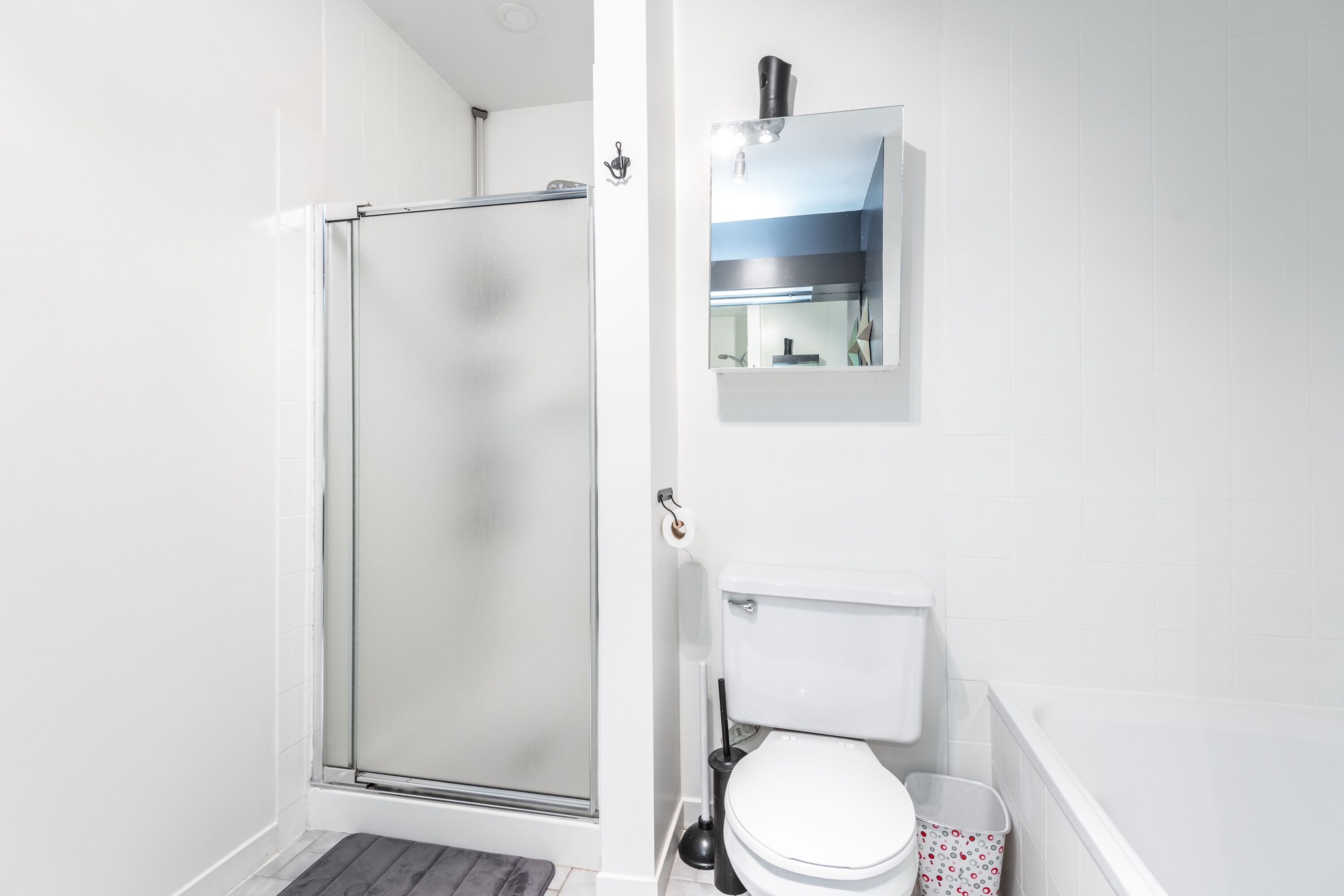 Ein modernes Badezimmer mit Duschkabine aus Glas, Toilette und Waschbecken mit Spiegel darüber.