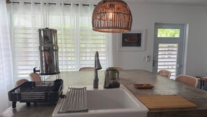 A kitchen with a white sink, stainless steel appliances, and a woven pendant light. - Casa Sandia- Ocean & Mountain Views- Home + Studio (Pastillas)