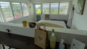 A room with a window view, a bed, a desk with a chair, and a small table with a bottle and a bag. - Casa Sandia- Ocean & Mountain Views- Home + Studio (Pastillas)