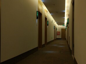 Un pasillo de hotel con pisos alfombrados, puertas y letreros direccionales verdes.