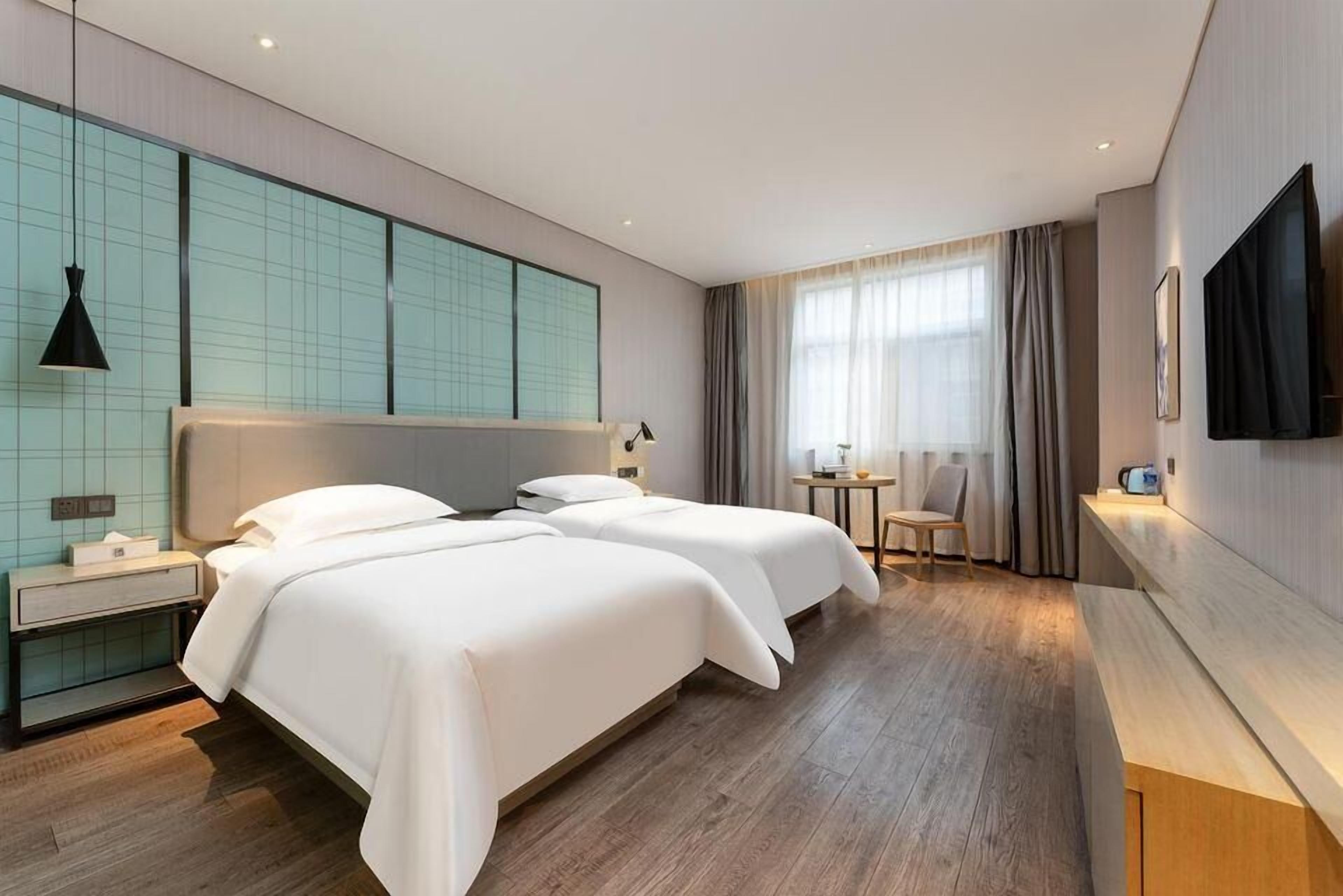 Een moderne hotelkamer met twee bedden, een nachtkastje, een televisie en een groot raam met gordijnen.