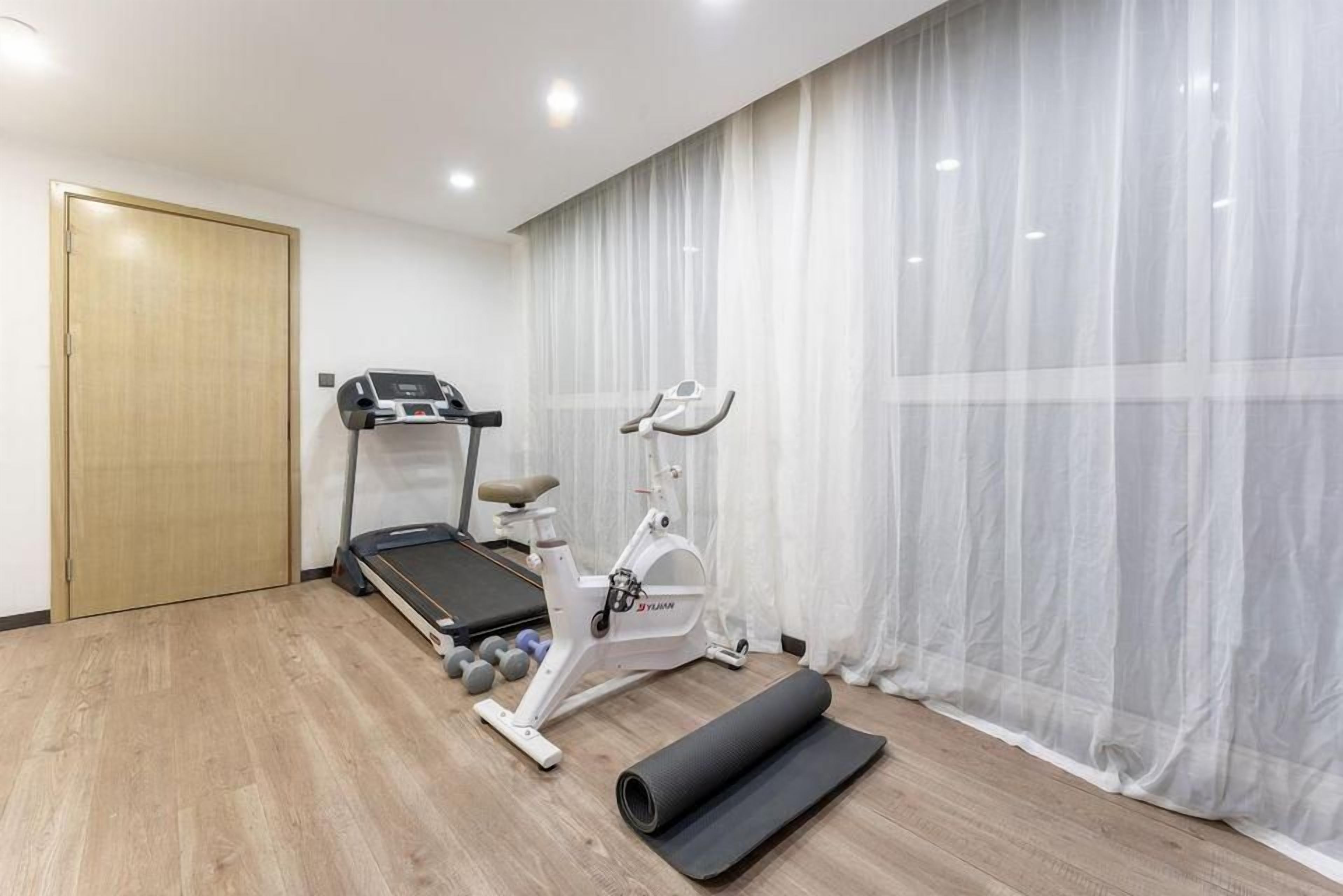 Een kamer met een loopband, een hometrainer en een yogamat.