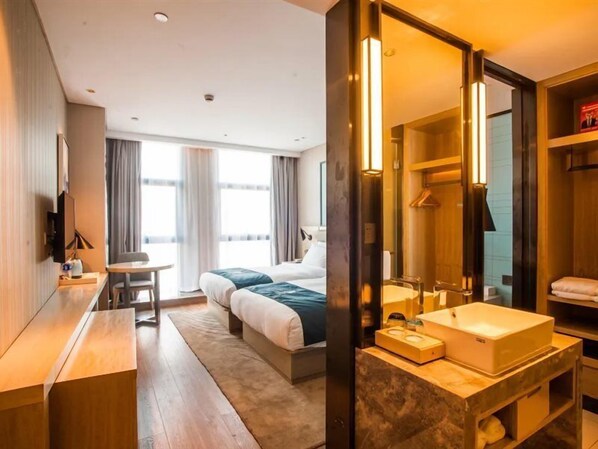 A hotel room with a bed, bedside table, mirror, and a bathroom with a sink and towel rack.