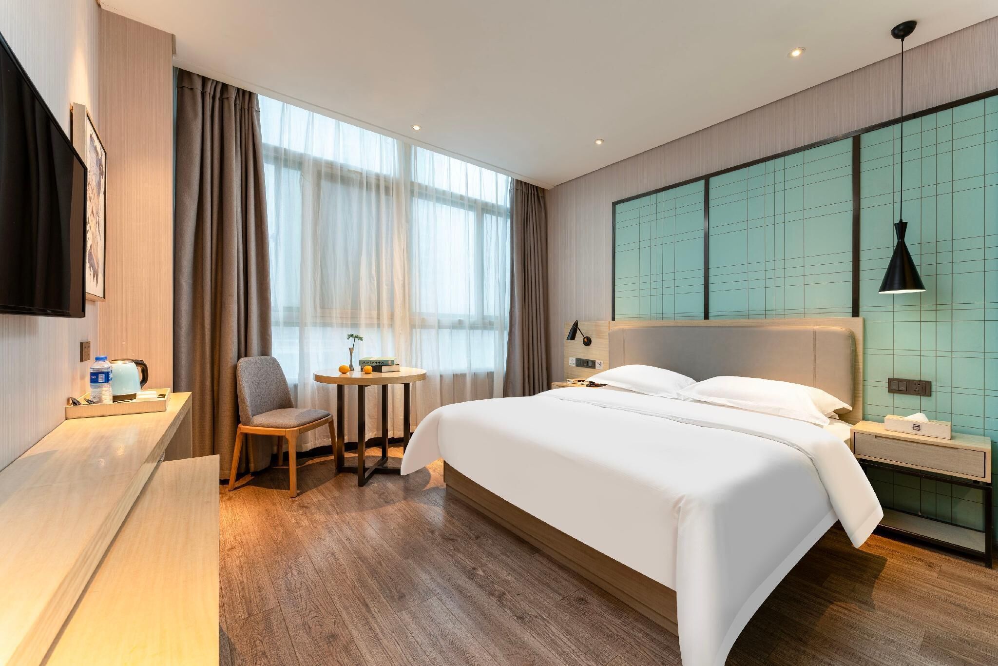 A modern hotel room with a large bed, a desk, a chair, and a TV.