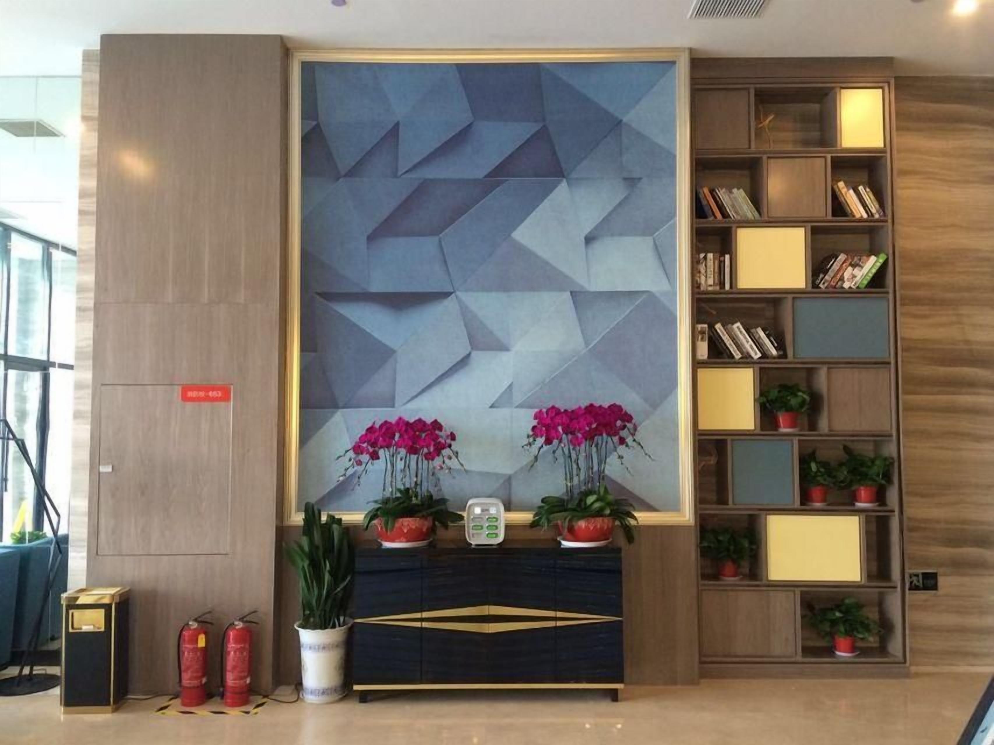 En moderne lobby med et geometrisk vægdesign, en reol og potteplanter.