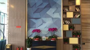 En moderne lobby med et geometrisk vægdesign, en reol og potteplanter.