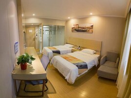 A hotel room with two beds, a desk, a chair, and a small table with a plant.