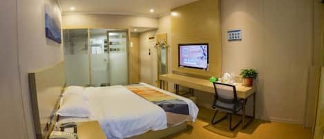 A hotel room with a bed, a desk with a chair, a television, and a small plant.