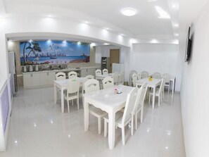 A dining area with white tables and chairs, a kitchen with a mural, and a flat-screen TV on the wall. - Shell Taian Dongping County Xishan Road Ruyuan City Square Dongyue Plaza (Tai'an)