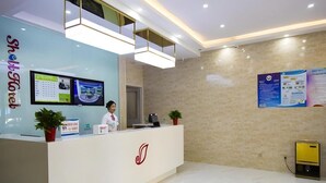 Zona de recepción de un hotel con diseño moderno, que incluye un mostrador de recepción, pantallas digitales y un suelo de baldosas limpias.