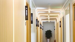 Pasillo de hotel con piso colorido, puertas numeradas y una planta en maceta en el centro.