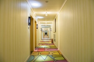 A hotel hallway with a colorful geometric carpet, light-colored walls, and a series of overhead lights.