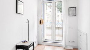 A room with a large sliding glass door, a small table with a book and sunglasses, a floor lamp, and a framed picture on the wall. - JOIVY Modern flat w/river view near Bica Elevator (Lisboa)