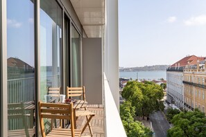 A balcony with wooden chairs and a table, overlooking a cityscape with buildings and a body of water. - JOIVY Amazing central studio w/river view in Lisbon (Lisboa)