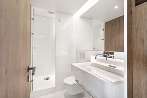 A modern bathroom with a glass shower enclosure, a white toilet, and a vanity with a mirror and sink. - JOIVY Amazing central studio w/river view in Lisbon (Lisboa)