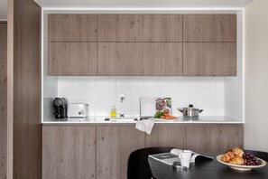 A modern kitchen with wooden cabinets, a white countertop, a coffee maker, a toaster, a kettle, and a bowl of croissants and grapes. - JOIVY Amazing central studio w/river view in Lisbon (Lisboa)