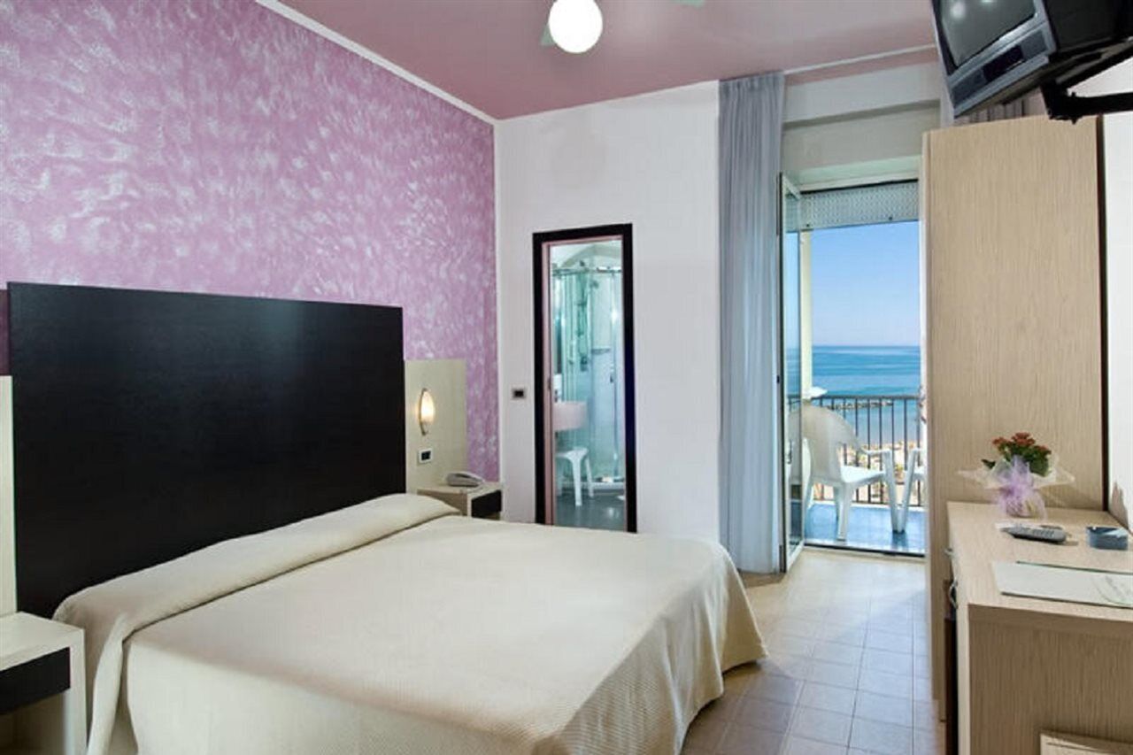 Ein Hotelzimmer mit Bett, Schreibtisch, Fernseher und einem Balkon mit Meerblick.